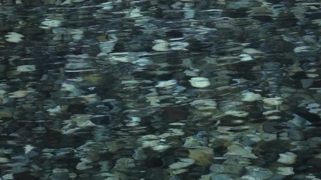 Slow motion, 240fps, of abstract natural background. Beautiful view for amazing intro in excellent eight times decelerated clip. Ripple on shallow transparent water surface with gray shingle bottom.