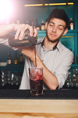 Young handsome barman pouring cocktail drink into glass