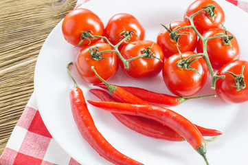 TTomatoes and red hot peppers on a white plate on a wooden table, close up. Raw ripe vegetables, ingredients for cooking on red white napkin.