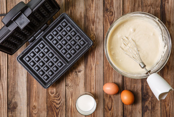 Making waffles at home - waffle iron, batter in bowl and ingredients - milk and eggs.