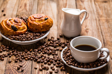 Coffee cup with milk jug and cinnabons on wooden background.