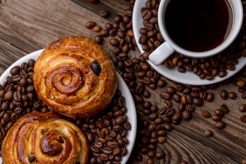 Coffee cup with cinnabons and coffee bean on wooden background.