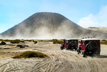 Two of off-road vehicle driving through the desert with beautiful volcano in background.