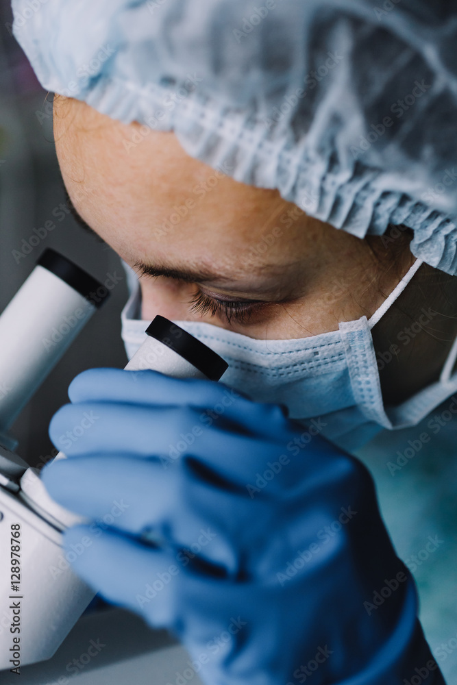 Wall mural from above view of young scientist in work uniform looking at microscope.
