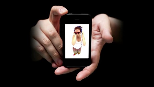 Mobile Phone Screen Shows Young Woman Listening Music and Dancing, wearing earphones and funny red heart shape glasses, studio shot on white background with fisheye lens