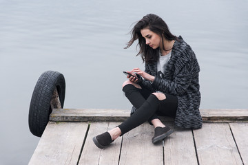 A young woman is using phone on the pier