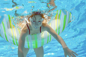 Obraz na płótnie Canvas Funny child swims in pool under water, kid having fun and playing with rubber ring, little girl on family vacation 