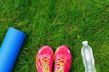 Fitness and healthy lifestyle concept, sport shoes, bottle of water and mat on grass background
