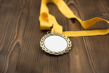 Gold medal with white placeholder and yellow ribbon on wooden textured table