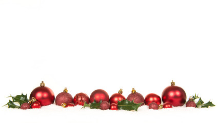 Row of red christmas ball decorations and green holly ilex in the snow on a white background