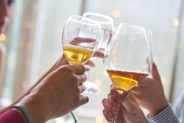 Clinking glasses of champagne in hands on bright lights background