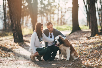 People and dogs. Young couple enjoying nature or park outdoors together with their  adorable Saint Bernard puppy.