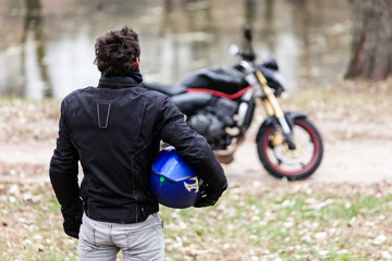 Biker standing near motorcycle, holding his blue helmet.