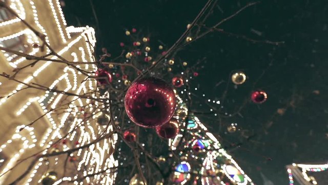 Christmas street decoration. Building, trees in garlands. Red and yellow decorative balls hanging on the trees against background with illuminated building. Beautiful Christmas Balls.