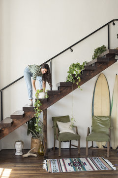 Young woman on stairs in a loft caring for potted plant