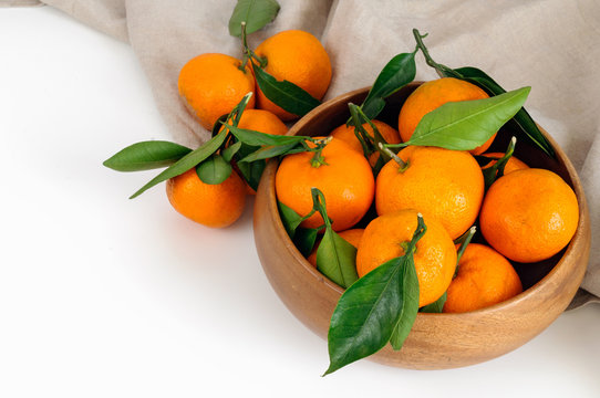 Fresh tangerines with green leaves in a wooden bowl