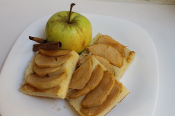 Delicious crumbly apple pie near garden apple with cinnamon stick on a white plate on a white...