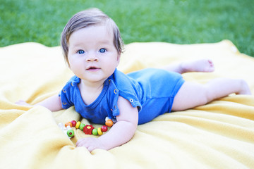 Newborn girl with blue eyes in the beautiful park outdoors, lies on a blanket wearing blue babybody and looking into camera

