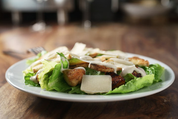 plate with fresh caesar salad with chicken on old wooden table, shallow focus
