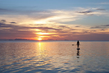 Fototapeta na wymiar Paddleboarding at sunset. Silhouette of a young woman with cloudy landscape on the background.