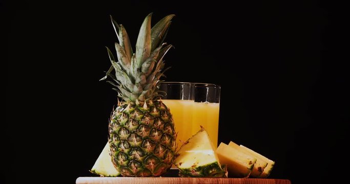 Still life pineapple juice fruits composition rotation 4k looped intro video copy space. Drink glass grocery food isolated on black background