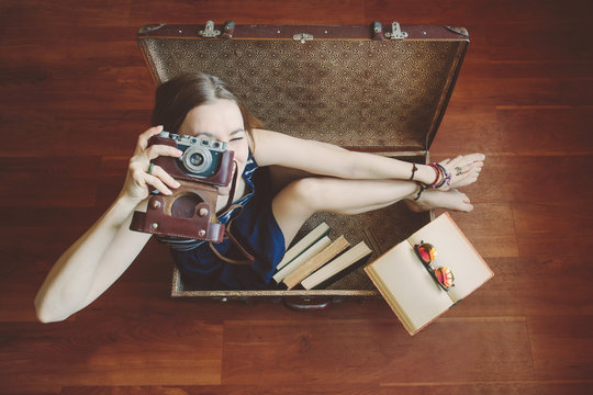 Young beautiful woman with retro camera sitting in big suitcase. Time to travel, luggage