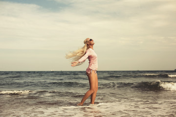 Fototapeta na wymiar Woman relaxing at beach enjoying summer freedom with open arms and hair in the wind by the water seaside. Caucasian girl on summer travel holidays vacation outside