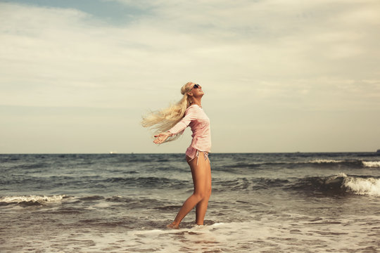 Woman relaxing at beach enjoying summer freedom with open arms and hair in the wind by the water seaside. Caucasian girl on summer travel holidays vacation outside