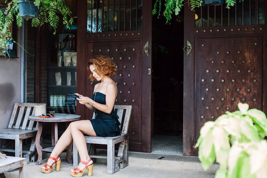 Young girl sitting in cafe outdoor and using phone gadget  for communication or shopping online