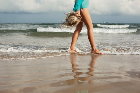 Walking on the beach. Close up on legs walking along the sea side, woman with straw hat enjoy freedom on beautiful ocean