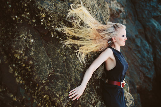 Art portrait of beautiful blond woman with long hair lying on big rocks
