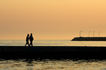 Fototapeta premium Grandpa and grandma on vacation walking on a pier by the sea at sunset in Chalkidiki, Greece