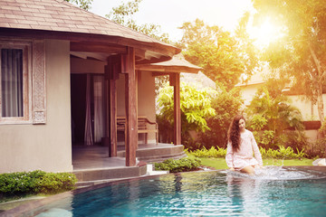 Beautiful woman sitting at swimming pool near luxury villa resort. Summer vacation