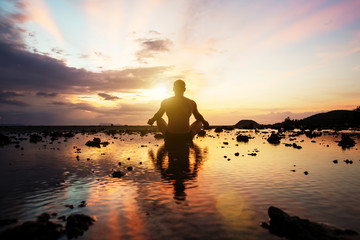 Silhouette of sitting young man practicing yoga on the beach at sunset