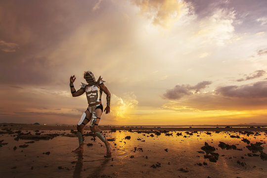Dancing male in fashion robot suit on beautiful sunset landscape on sea shore