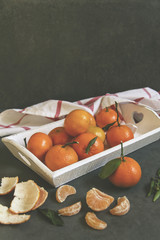 Tangerines, clementines on white tray. Gray background, white kitchen towel.