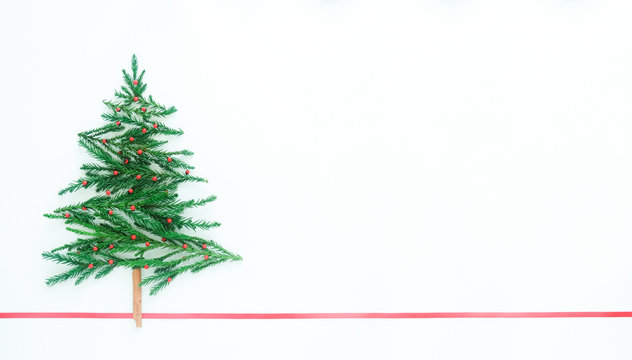 Christmas tree made from pine leaves, cinnamon, red seed on white background and red ribbon line, copy space