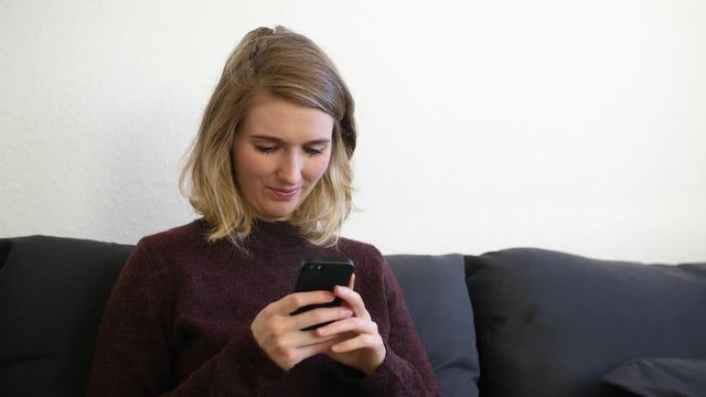 Junge europ&auml;ische Frau sitzt auf dem Sofa und tippt auf dem Handy