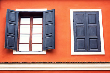 Detail of an open wooden iron vintage rustic windows on red cement old wall can be used for background. Brown black window shutters with decorative flowers