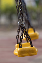 Empty yellow plastic swings on modern playground with selective focus