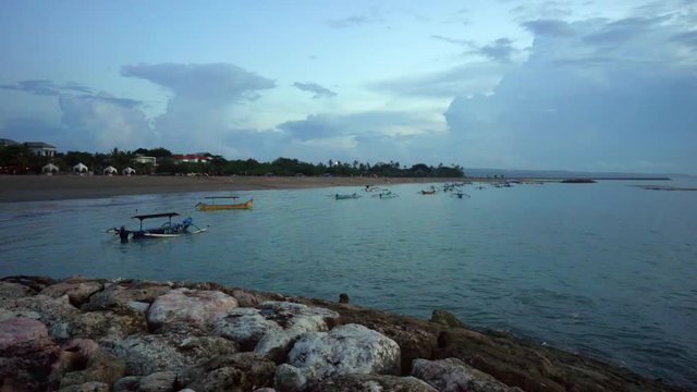 Evening seascape on Bali. Indonesia. Front view on seashore with stones and boats in ocean. Wide angle.