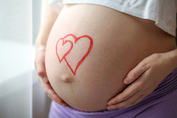 Young pregnant woman holding and touching her belly, closeup
