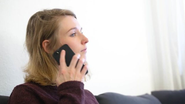 Junge europ&auml;ische Frau sitzt auf dem Sofa und telefoniert mit dem Handy