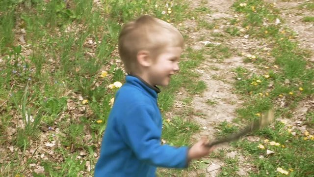 Happy little 3-5 years child boy looks at camera laughs and smiles runs and plays outdoor game with rod. Carefree childhood summer and happiness concept.