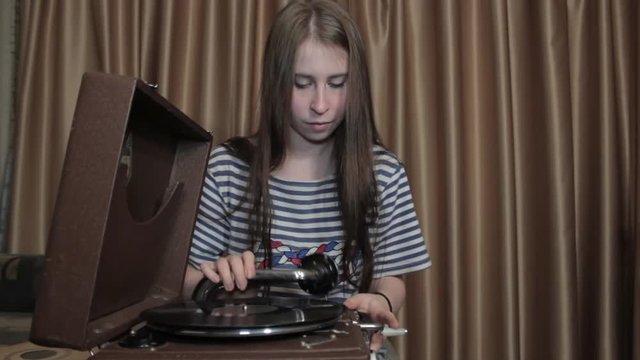 Girl Listens to Phonograph. Girl turns the handle of the gramophone and listening to music from gramophone records
