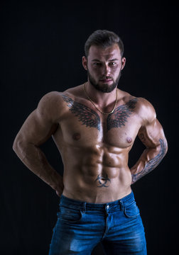 Handsome shirtless muscular man with jeans, standing, on black background