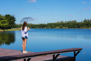 Fototapeta na wymiar Woman holding an umbrella stand, a pond and watching nature.