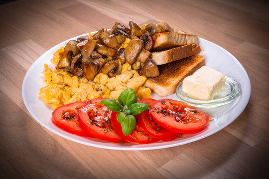 Breakfast table with crambled eggs, mashrooms and tomatoes on the plate