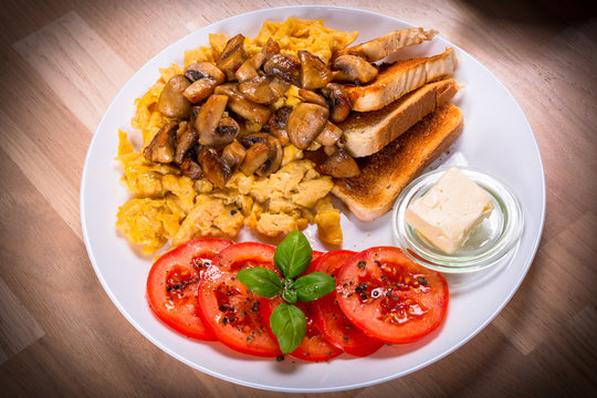 Breakfast table with crambled eggs, mashrooms and tomatoes on the plate