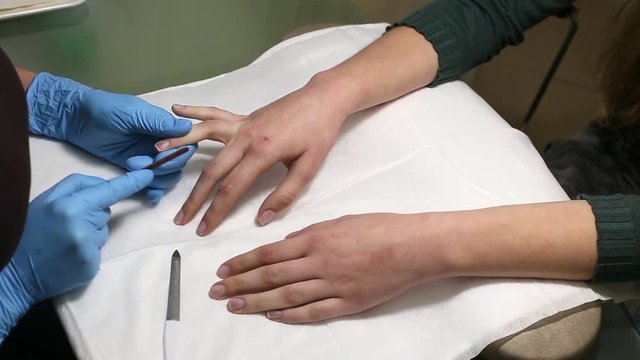 manicurist makes the manicure for young caucasian woman in beauty salon. hands close up